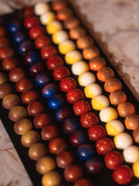 Rows of round, glossy chocolates or candies in blue, red, yellow, white, and brown are arranged neatly on a black tray—perfect for sophisticated Napa Valley events.