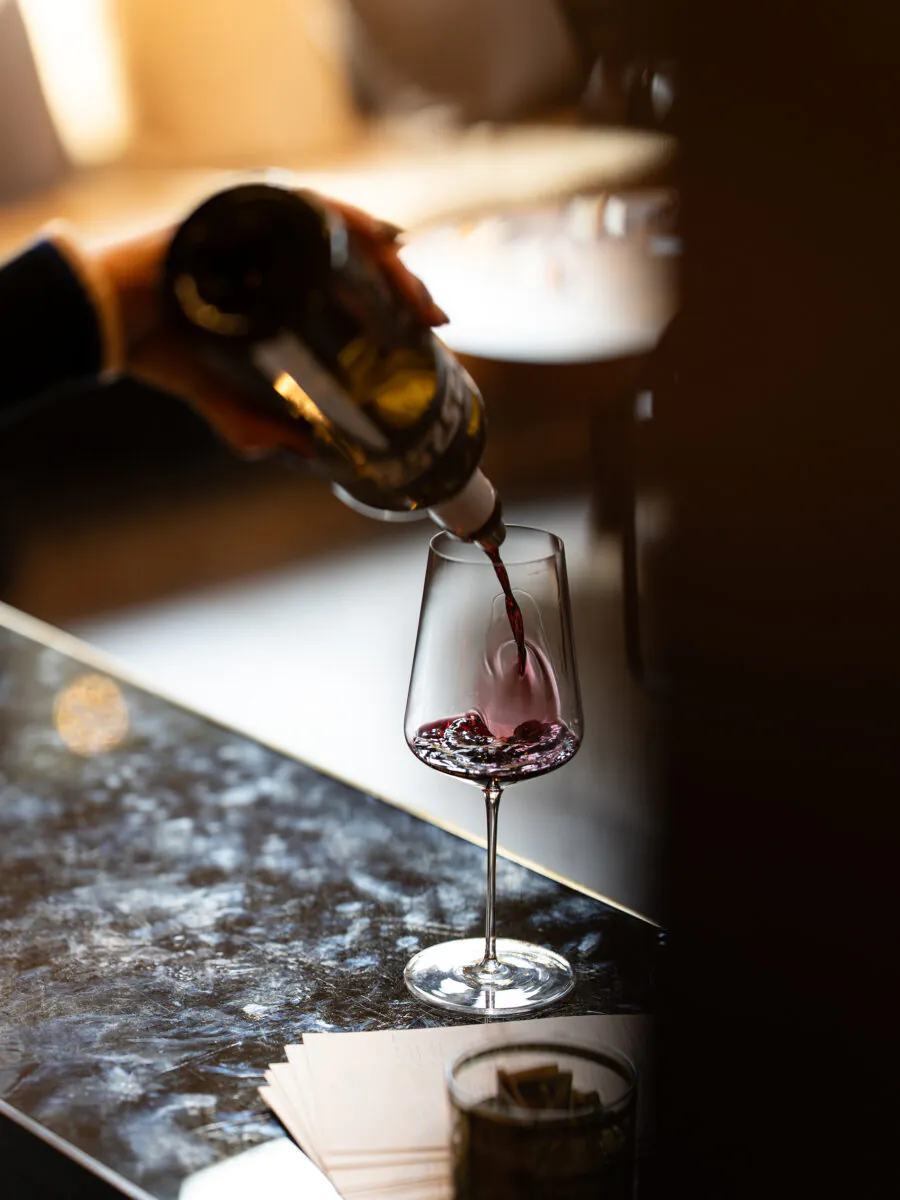 A hand pours red wine from a bottle into a wine glass on a marble countertop, with some papers visible nearby—perfect inspiration for planning your next Napa Valley Events gathering.
