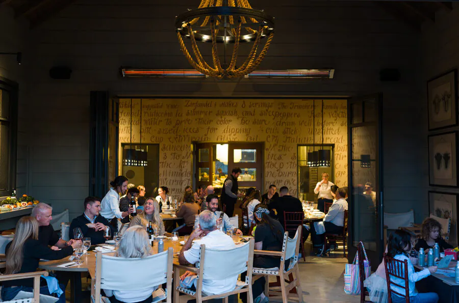 People dining at a restaurant, seated at tables in a warmly lit room with a chandelier and decorative writing on the wall—perfect for memorable Napa Valley Events.
