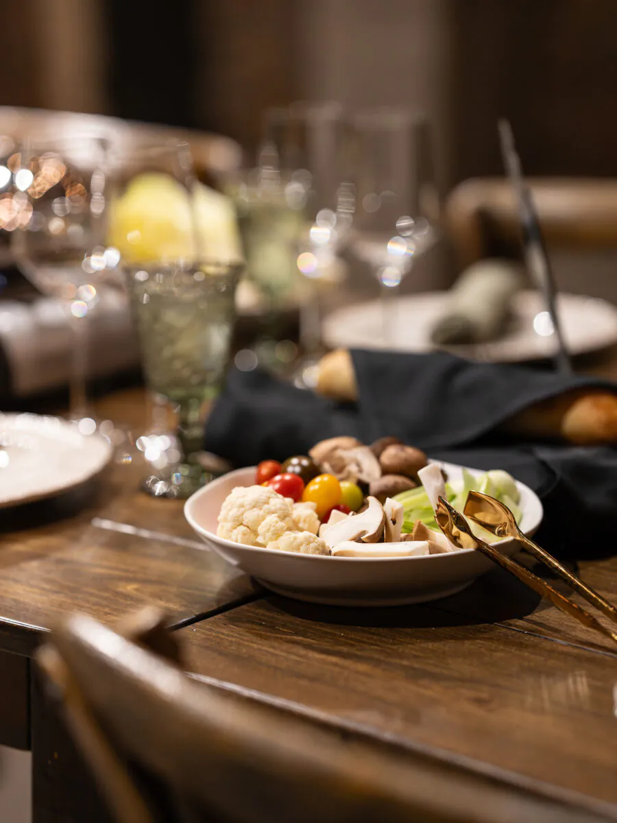 A plate of assorted raw vegetables with gold utensils sits on a wooden dining table set for Napa Valley Events, complete with elegant glassware, napkins, and bread.